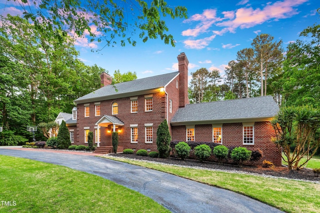 view of front of property featuring a lawn, brick siding, a chimney, and aphalt driveway