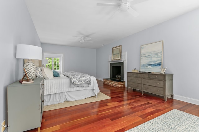bedroom with baseboards, a fireplace with raised hearth, ceiling fan, and wood finished floors