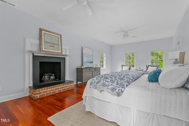 bedroom with visible vents, a brick fireplace, wood finished floors, baseboards, and a ceiling fan