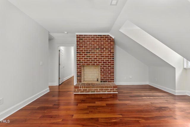 additional living space featuring vaulted ceiling with skylight, baseboards, a fireplace, and wood finished floors