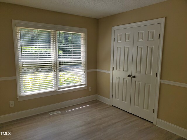 725 Van Thomas Dr, Raleigh, NC 27615 - unfurnished bedroom featuring a closet, wood finished floors, multiple windows, baseboards, and a textured ceiling