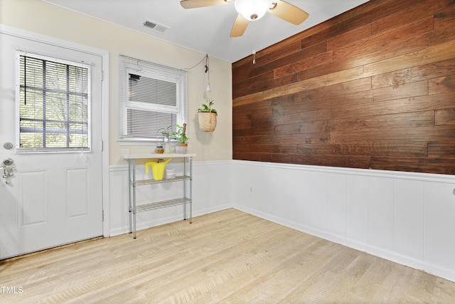interior space featuring visible vents, wood walls, light wood-style floors, a wainscoted wall, and a ceiling fan