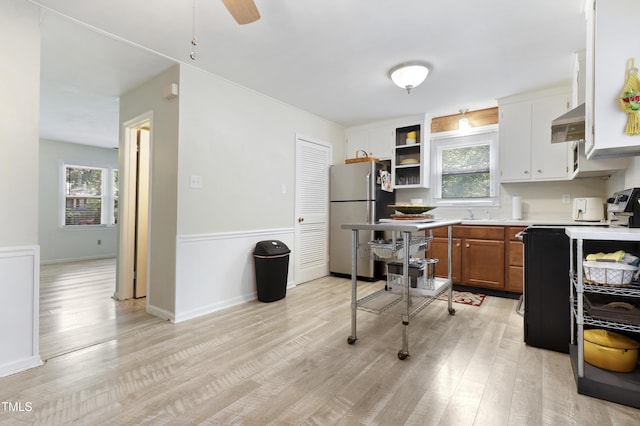 kitchen featuring brown cabinetry, freestanding refrigerator, light wood-type flooring, light countertops, and under cabinet range hood