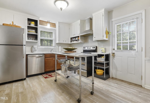 kitchen with open shelves, wall chimney exhaust hood, appliances with stainless steel finishes, and light wood finished floors