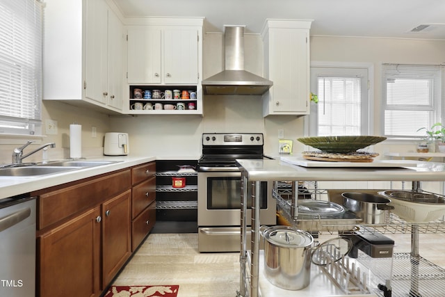 kitchen featuring wall chimney range hood, white cabinets, appliances with stainless steel finishes, a sink, and light countertops