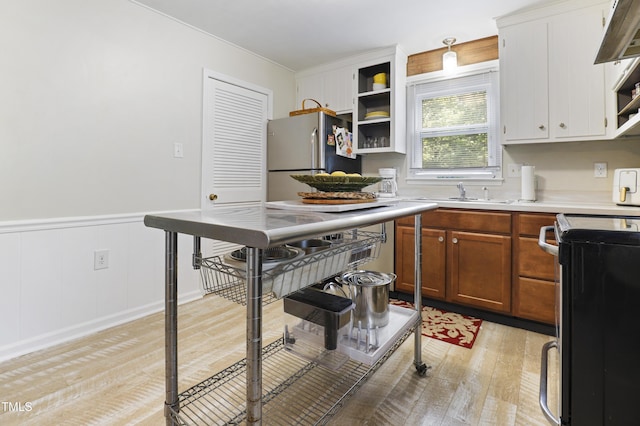 kitchen with open shelves, light countertops, a sink, freestanding refrigerator, and light wood finished floors