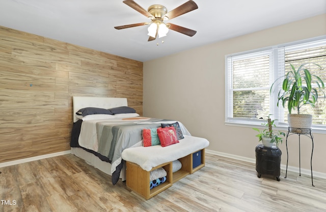 bedroom featuring baseboards, wood walls, ceiling fan, and wood finished floors
