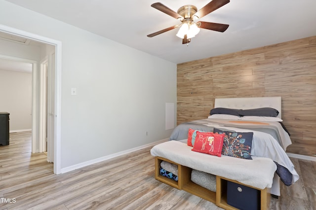bedroom featuring wood walls, an accent wall, a ceiling fan, baseboards, and wood finished floors
