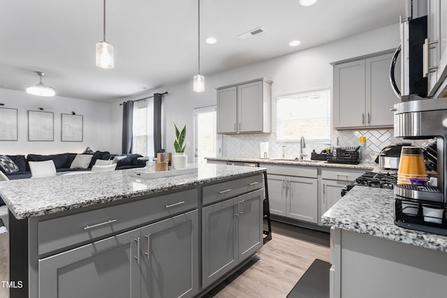 kitchen with a sink, gray cabinets, visible vents, backsplash, and open floor plan