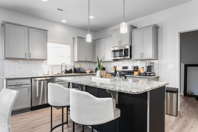 kitchen featuring a center island, gray cabinetry, light stone countertops, and appliances with stainless steel finishes