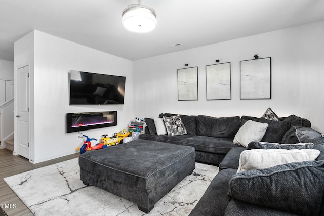 living room featuring visible vents, baseboards, wood finished floors, and a glass covered fireplace