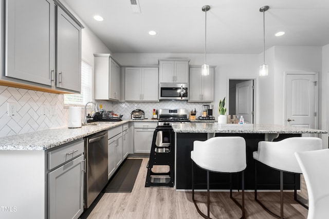 kitchen with a sink, gray cabinetry, stainless steel appliances, a kitchen island, and a kitchen bar