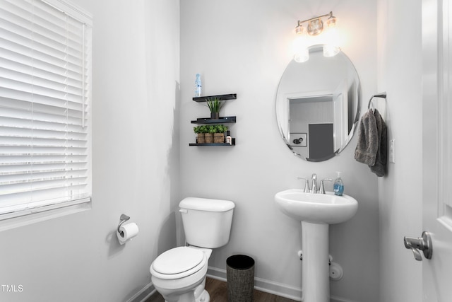 half bathroom with toilet, a sink, wood finished floors, and baseboards
