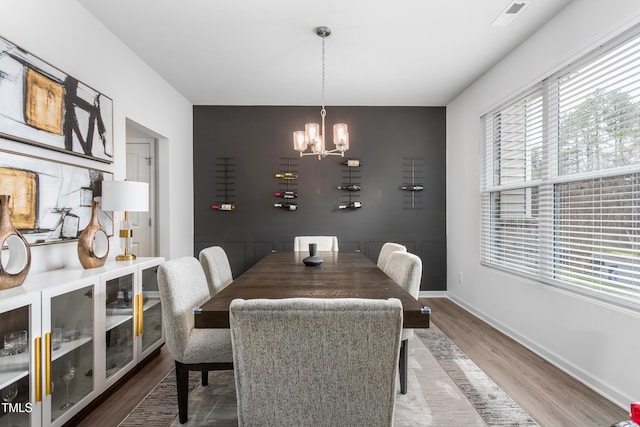 dining room with a notable chandelier, visible vents, wood finished floors, and baseboards