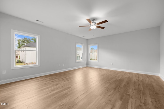unfurnished room with a ceiling fan, plenty of natural light, wood finished floors, and baseboards