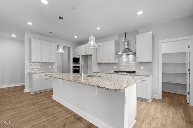 kitchen with wall chimney range hood, a sink, tasteful backsplash, stainless steel appliances, and a center island with sink