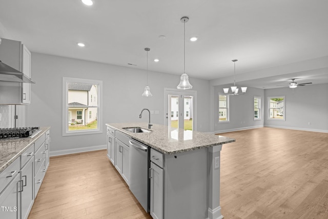 kitchen featuring stainless steel appliances, a sink, light wood-style flooring, baseboards, and light stone countertops