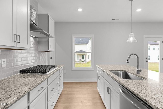 kitchen featuring a sink, appliances with stainless steel finishes, light wood-type flooring, backsplash, and wall chimney range hood