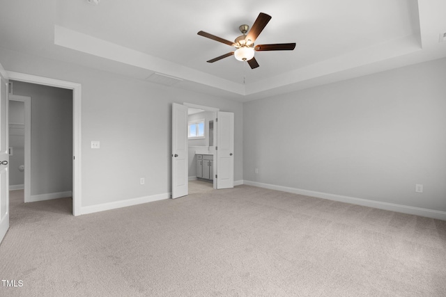 unfurnished bedroom featuring a raised ceiling, light colored carpet, baseboards, and a ceiling fan