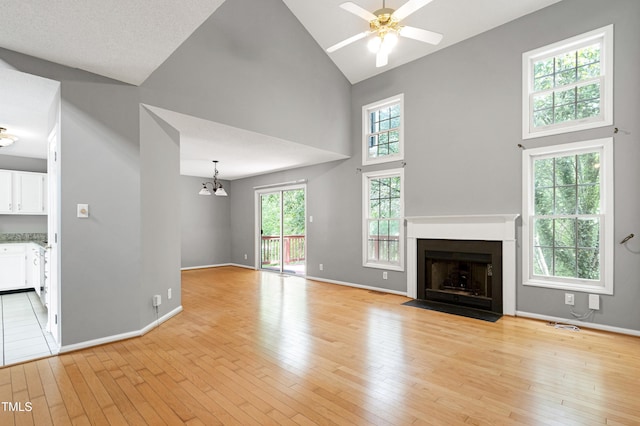 unfurnished living room featuring a fireplace with flush hearth, light wood-type flooring, baseboards, high vaulted ceiling, and ceiling fan with notable chandelier