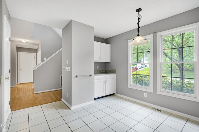 kitchen with white cabinets, baseboards, visible vents, light tile patterned floors, and hanging light fixtures