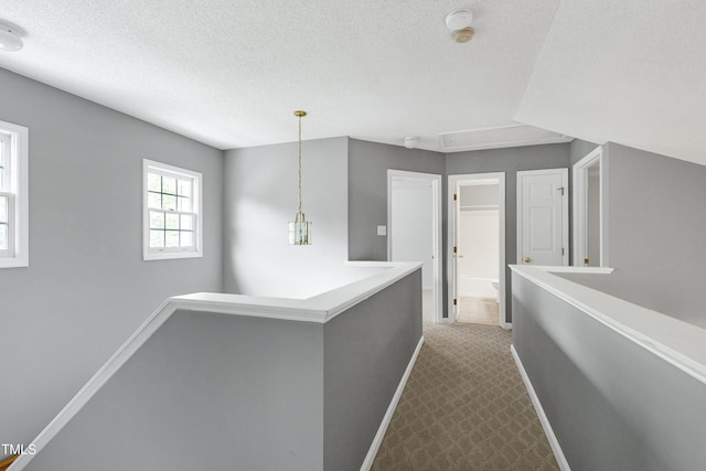 corridor with carpet floors, a textured ceiling, baseboards, and an upstairs landing