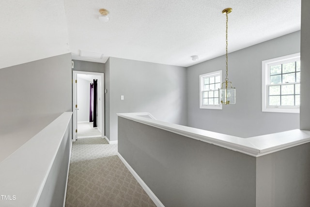 corridor featuring dark carpet, baseboards, an upstairs landing, and a textured ceiling