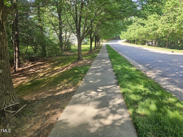 view of road featuring curbs, sidewalks, and a wooded view