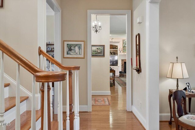 1317 Colonial Club Rd, Wake Forest, NC 27587 - hall featuring stairs, light wood finished floors, baseboards, and an inviting chandelier