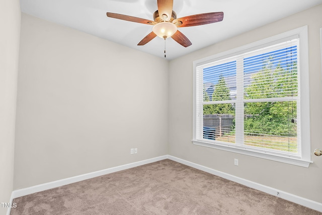 carpeted spare room featuring baseboards and a ceiling fan