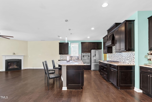 kitchen with appliances with stainless steel finishes, ceiling fan, dark brown cabinets, premium range hood, and open floor plan
