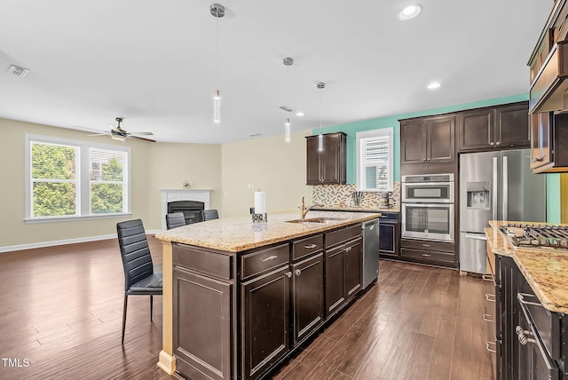 kitchen featuring dark wood finished floors, appliances with stainless steel finishes, a glass covered fireplace, a sink, and open floor plan