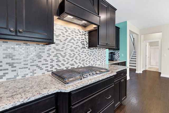 kitchen featuring tasteful backsplash, stainless steel gas cooktop, light stone counters, baseboards, and premium range hood