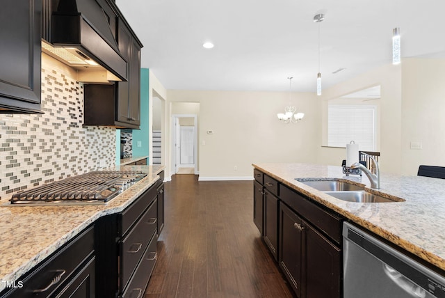 kitchen featuring a sink, stainless steel appliances, a notable chandelier, light stone counters, and backsplash