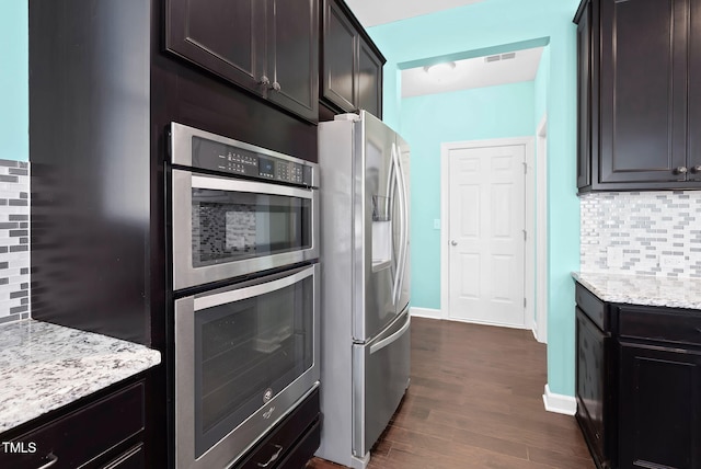 kitchen with light stone counters, visible vents, stainless steel appliances, dark wood-type flooring, and backsplash