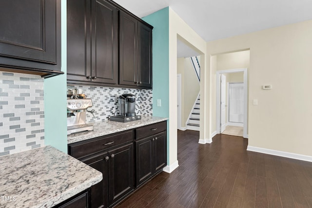 kitchen with light stone countertops, decorative backsplash, dark brown cabinets, baseboards, and dark wood-style floors