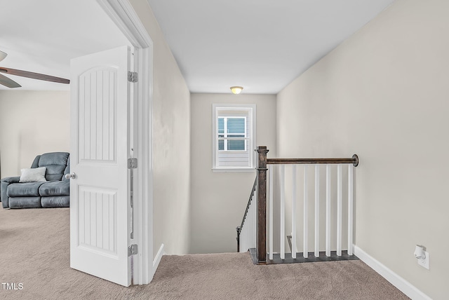hall with an upstairs landing, carpet floors, and baseboards