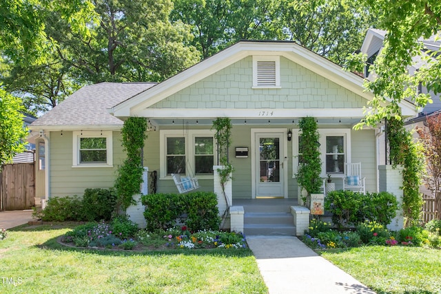 view of front of property featuring covered porch, fence, and a front lawn