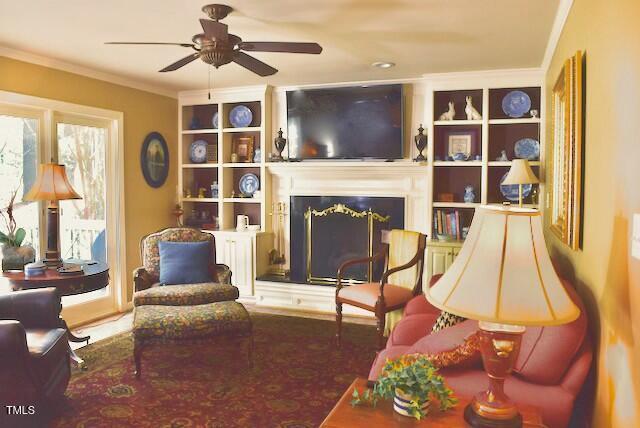 775 Sid Eaves Rd, Youngsville, NC 27596 - sitting room with a fireplace, a ceiling fan, built in shelves, and ornamental molding