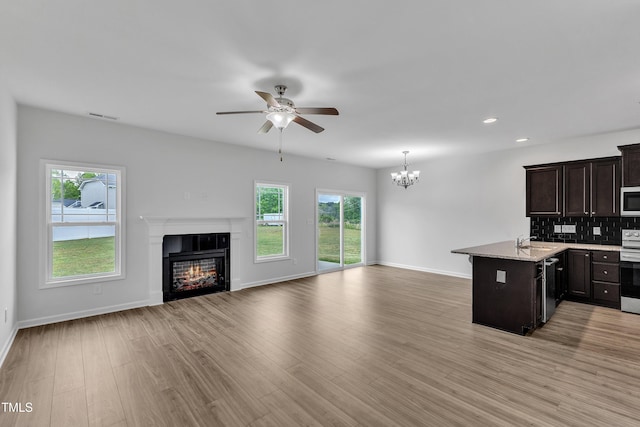 kitchen with appliances with stainless steel finishes, a sink, baseboards, open floor plan, and a glass covered fireplace