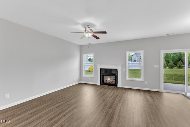 unfurnished living room with a glass covered fireplace, ceiling fan, dark wood finished floors, and a wealth of natural light