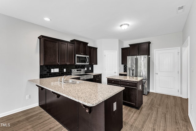 kitchen featuring dark brown cabinets, a sink, stainless steel appliances, baseboards, and wood finished floors