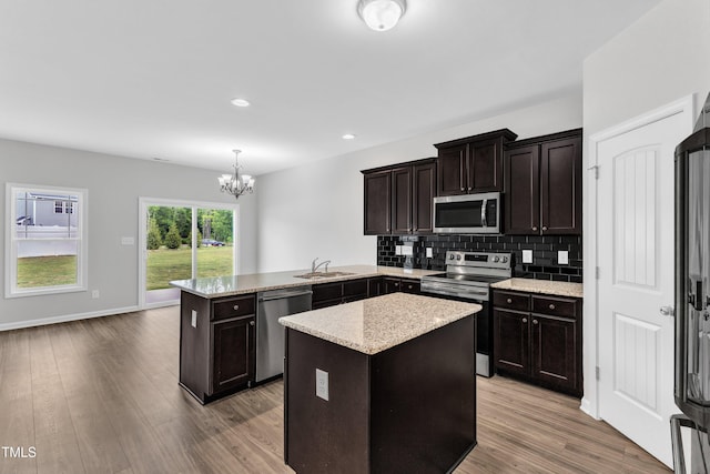 kitchen featuring appliances with stainless steel finishes, an inviting chandelier, a sink, light wood-style flooring, and a peninsula