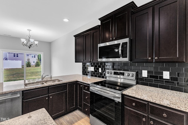 kitchen with a notable chandelier, appliances with stainless steel finishes, a sink, light wood-style floors, and tasteful backsplash
