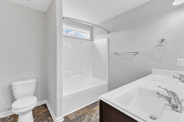 bathroom with a sink, baseboards, toilet, stone tile flooring, and  shower combination