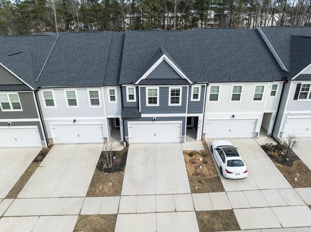 multi unit property with a shingled roof, driveway, and an attached garage