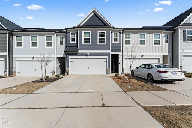 townhome / multi-family property featuring a garage, stone siding, concrete driveway, and board and batten siding