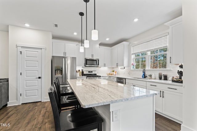 kitchen featuring stainless steel appliances, a sink, dark wood-type flooring, a kitchen island, and white cabinetry