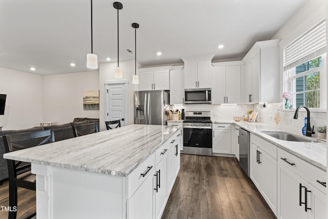 kitchen with stainless steel appliances, a sink, a kitchen island, light stone counters, and recessed lighting