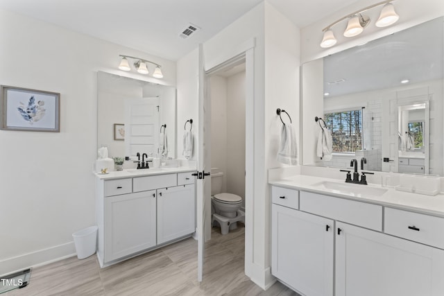 full bath with toilet, two vanities, and baseboards